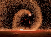 A fire performer twirling flaming batons, creating trails of light against the night sky.