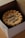 A round cake inside a box, decorated with light brown frosting along the edges and the message 'Happy New Year!' written in dark icing on top.