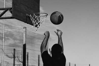 Black and white image of a basketball player soaring for a slam dunk against a dark backdrop.