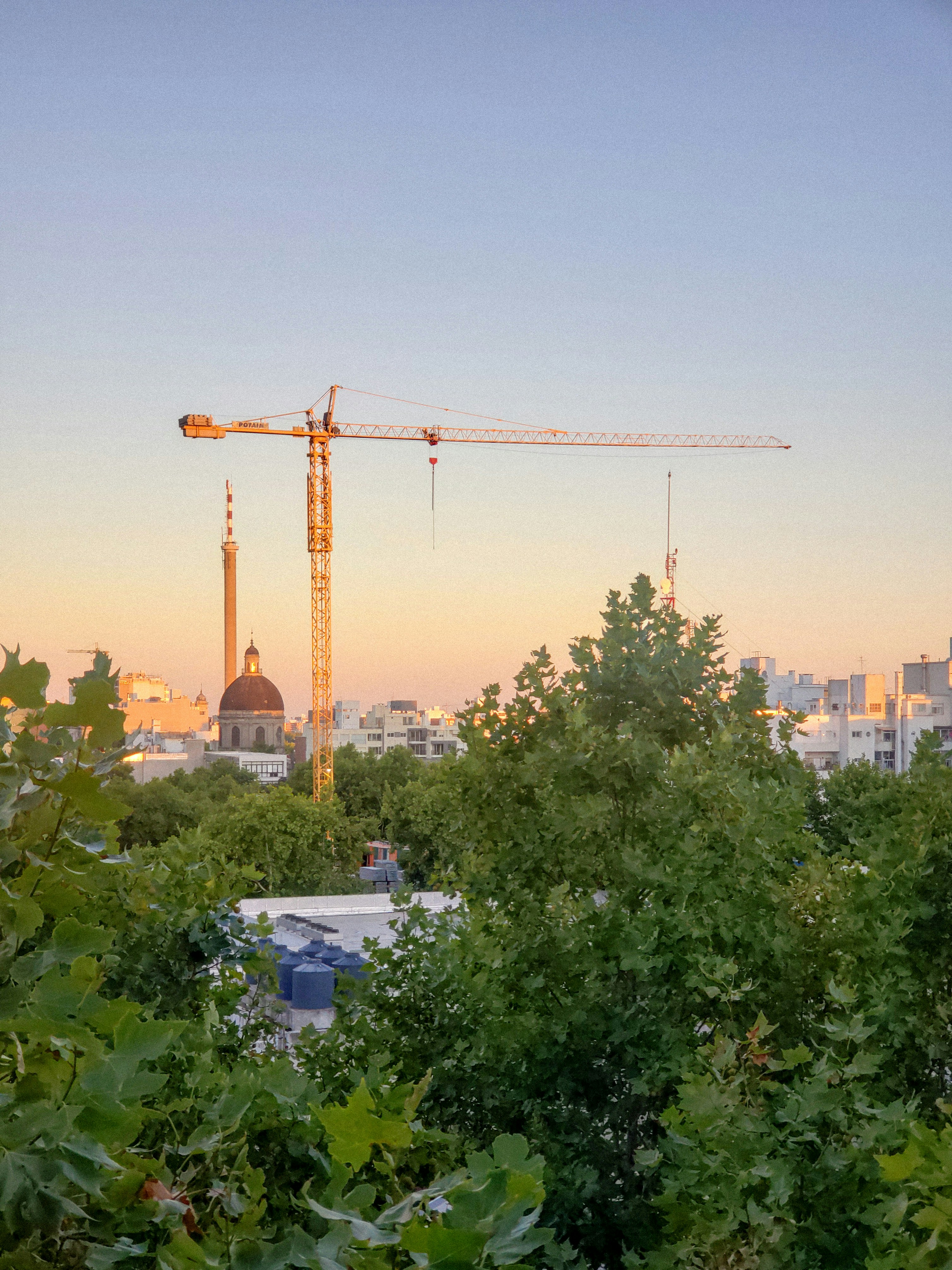 Construction site with dramatic overhead crane, golden hour light, industrial scale, deep shadow contrast