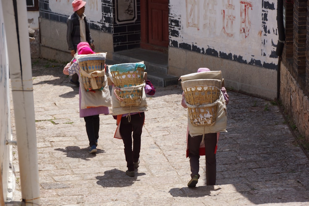 three people walking down a street carrying baskets