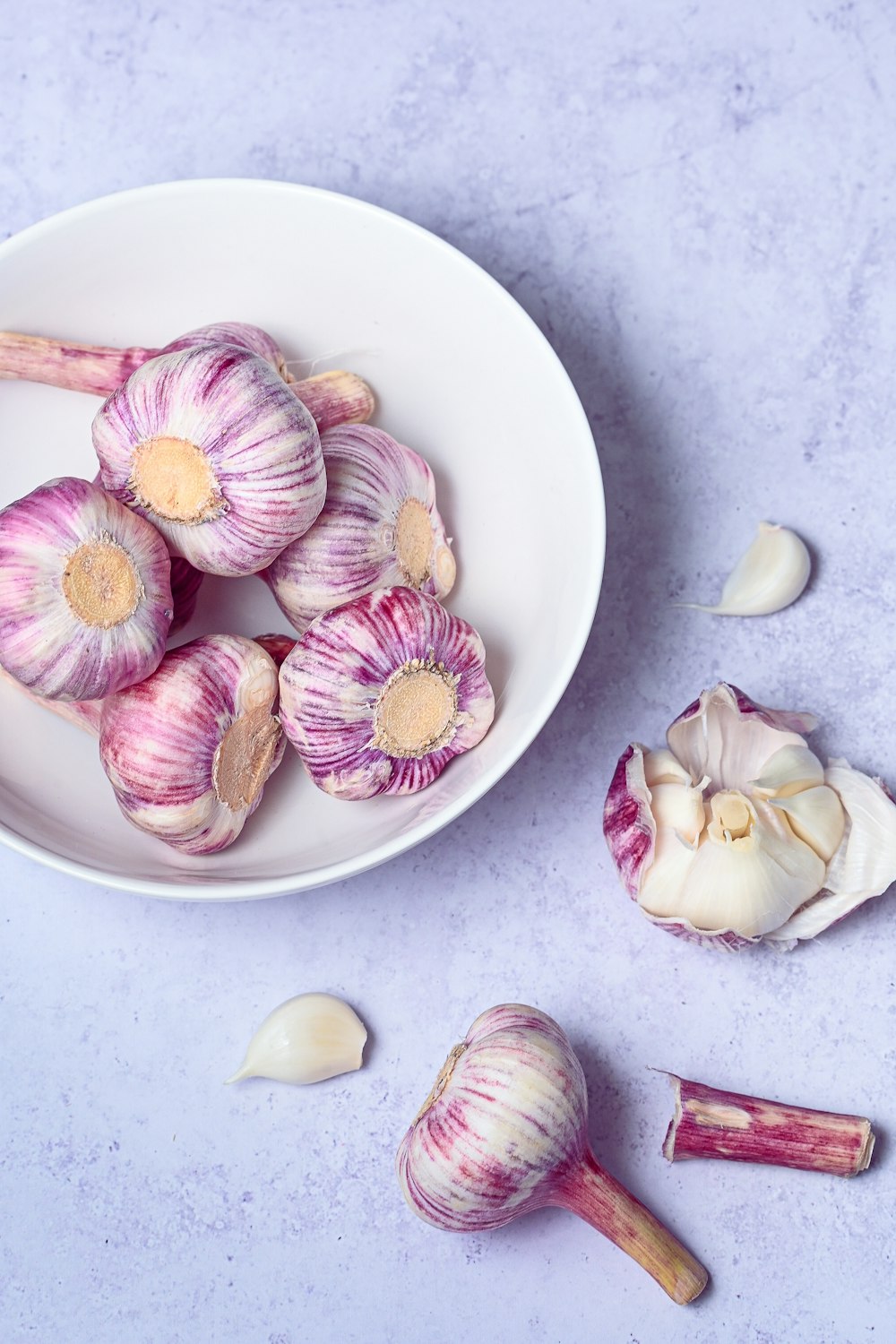 a white bowl filled with garlic next to a pile of garlic