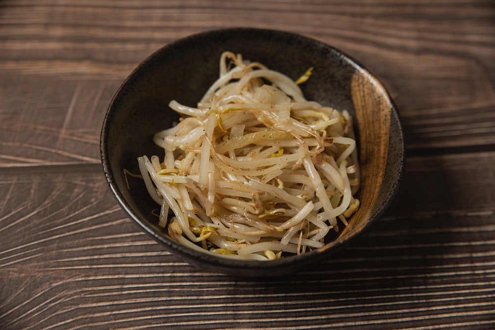 a black bowl filled with noodles on top of a wooden table