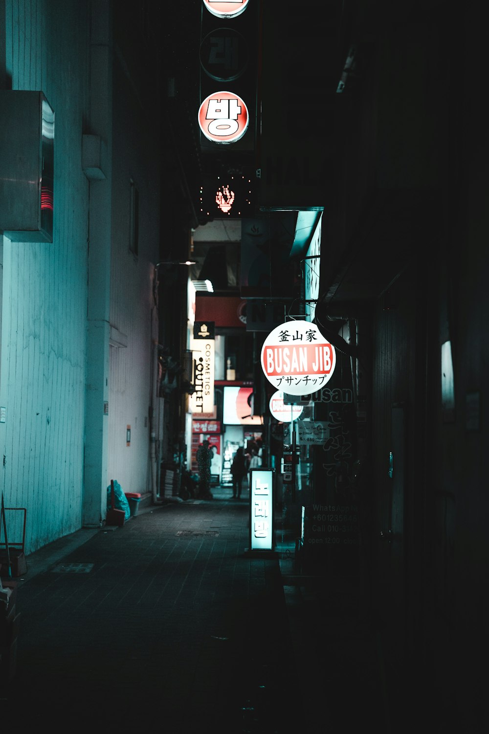 a dark alley with neon signs and a person sitting on a bench