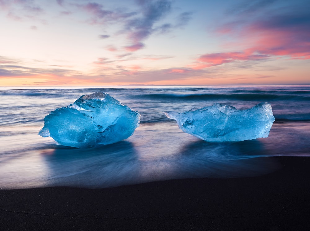 two icebergs sitting on top of a beach next to the ocean