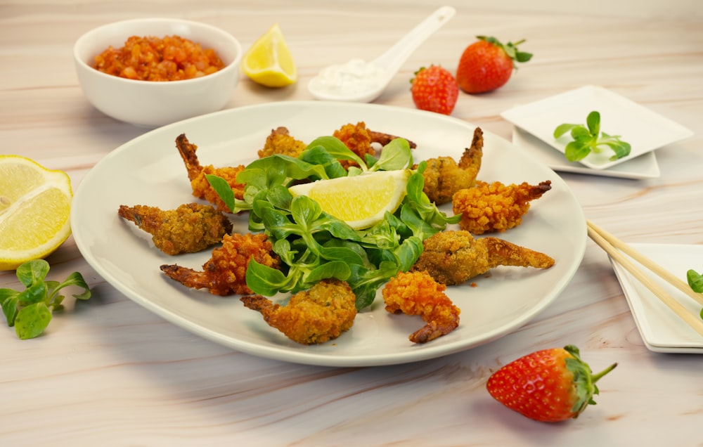 a white plate topped with fried shrimp next to a bowl of strawberries