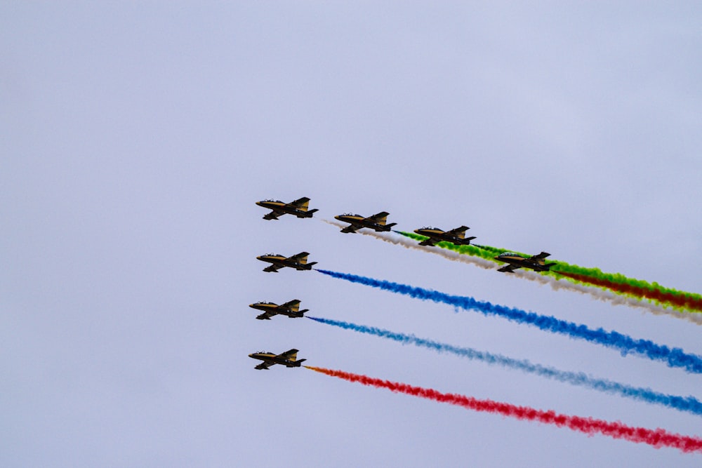 a group of airplanes flying in formation with colored smoke behind them