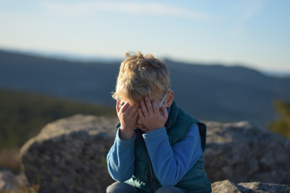 a young boy sitting on top of a large rock