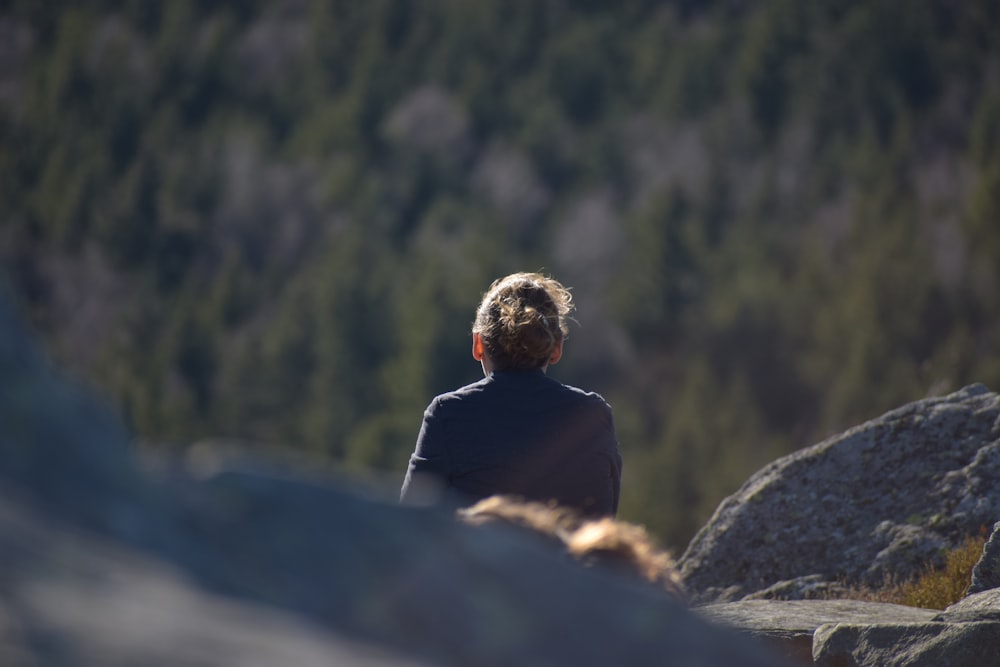 a man sitting on top of a rock next to a forest