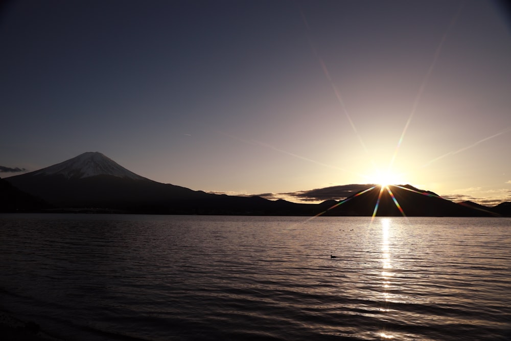 the sun is setting over a lake with a mountain in the background