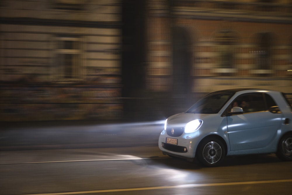 a small car driving down a street at night