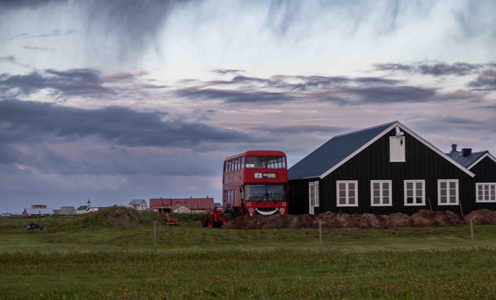 a red double decker bus driving past a black house