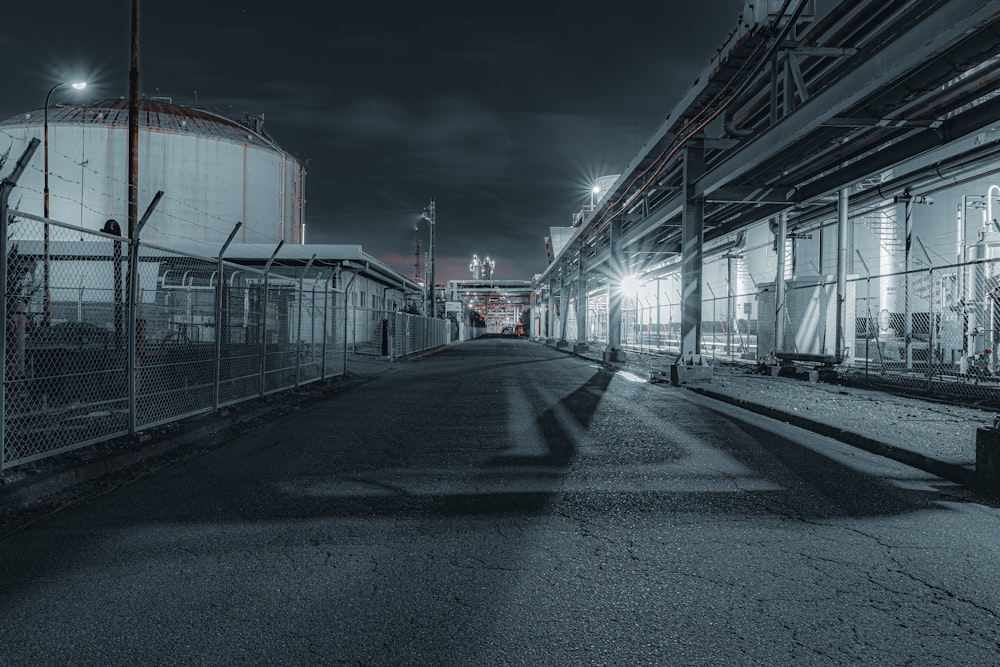 a dark street with a large industrial building in the background