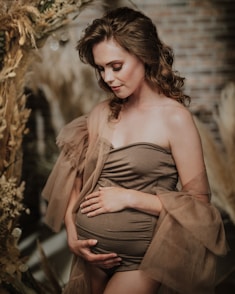 a pregnant woman in a brown dress poses for a photo