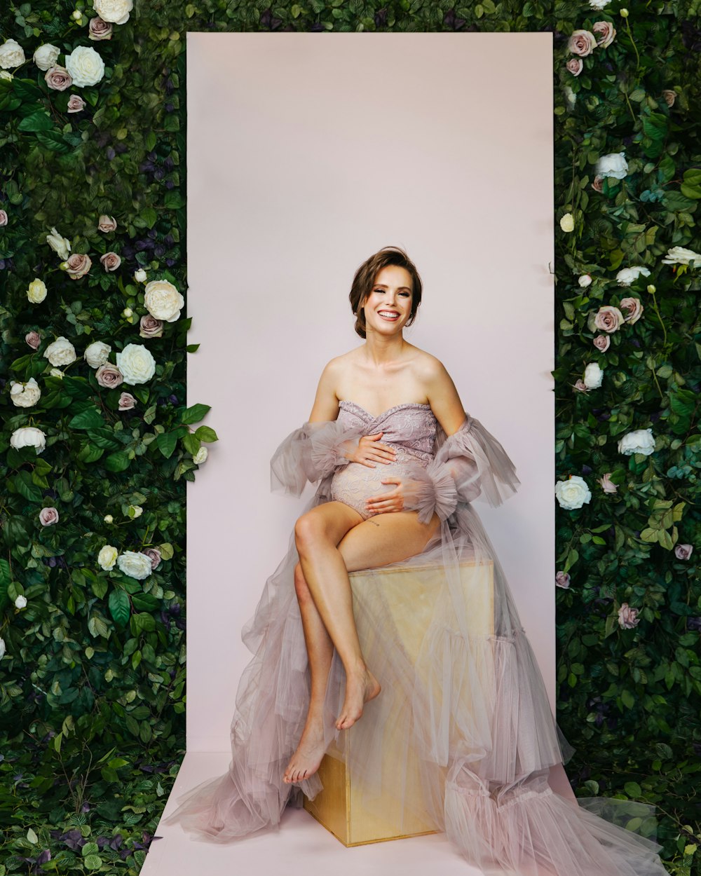 a pregnant woman sitting on a stool in front of a floral wall