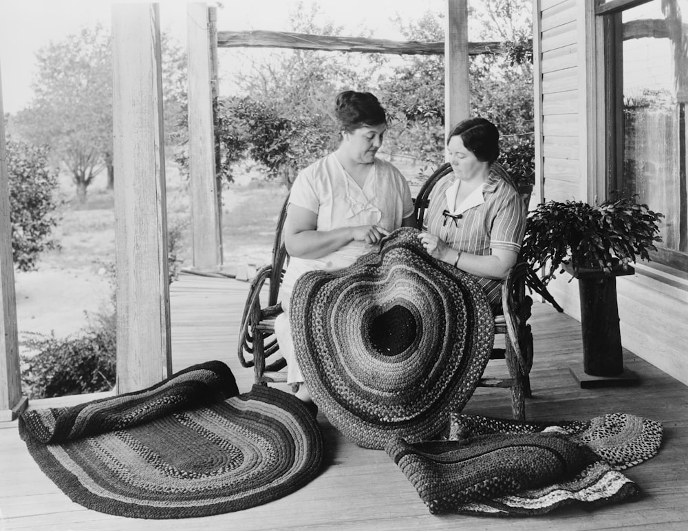 Two women making braided rugs on porch