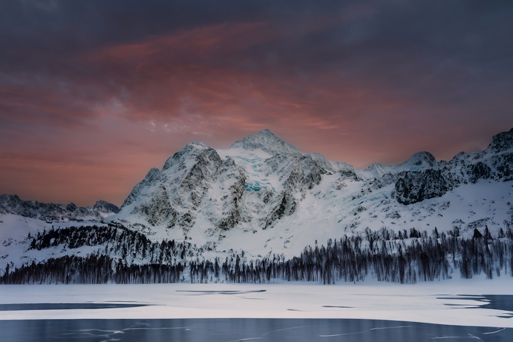 a mountain covered in snow next to a lake