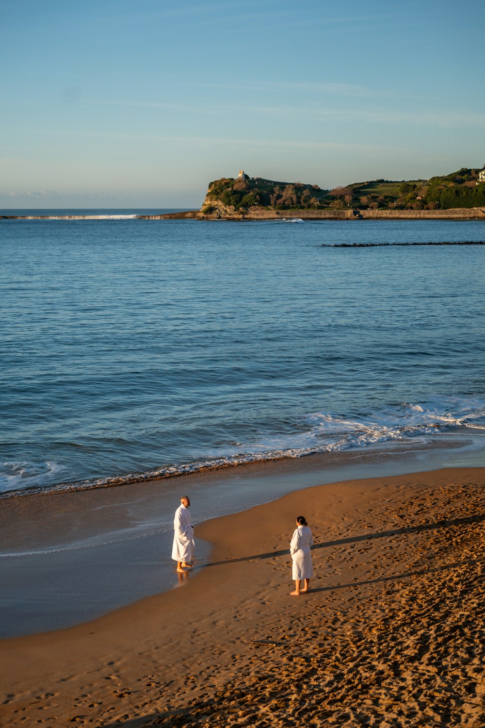 two people walking on a beach next to the ocean