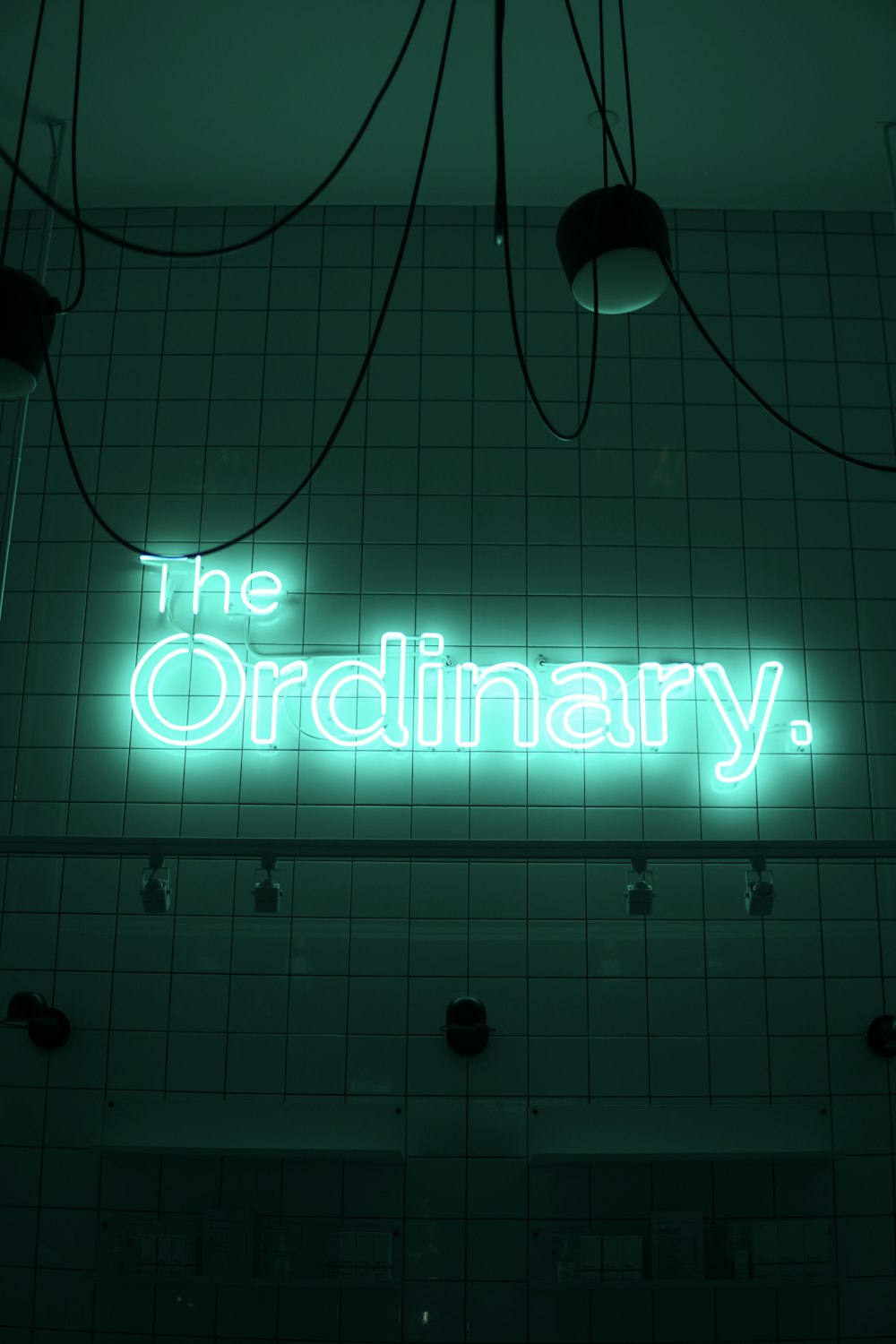 a neon sign that reads the ordinary above a tiled wall