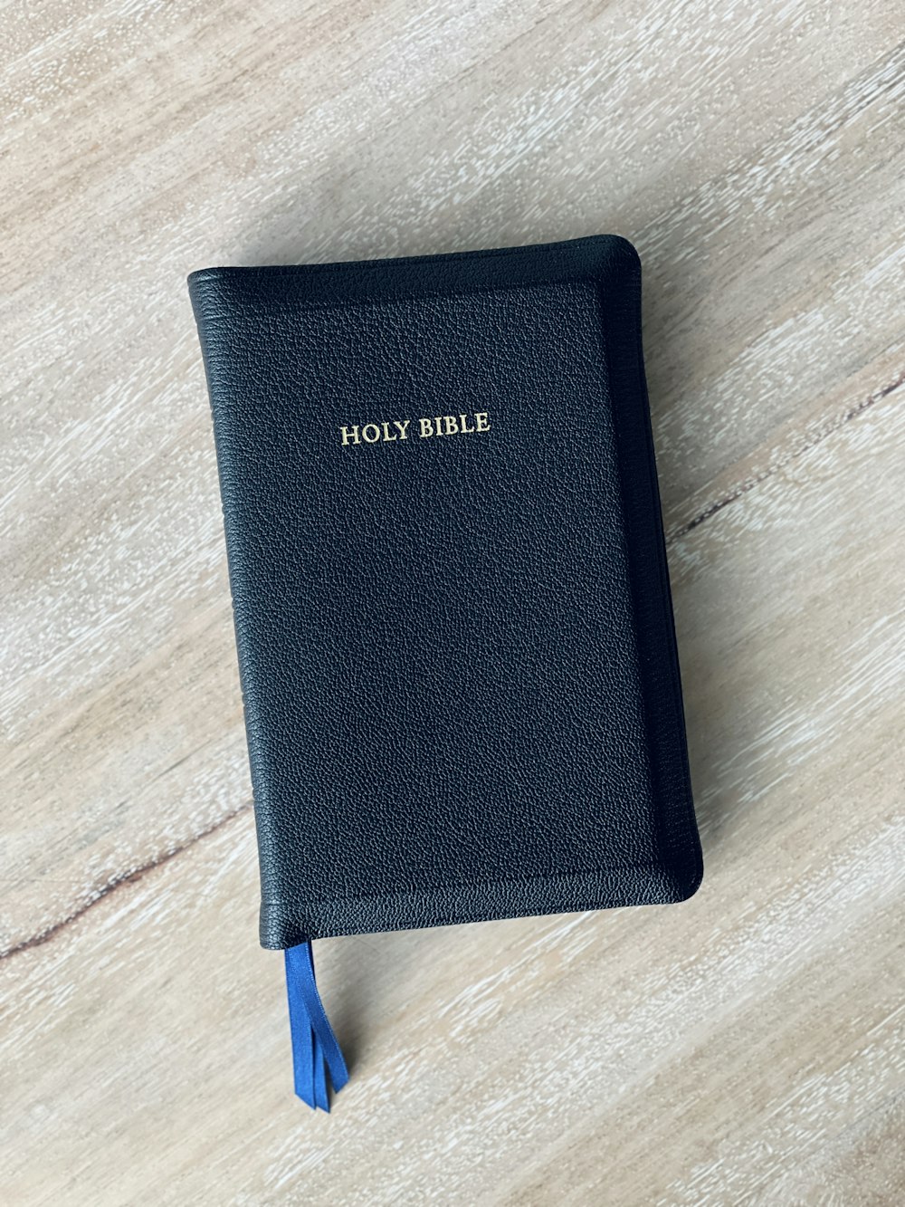 a black bible on a wooden table with a blue tassel