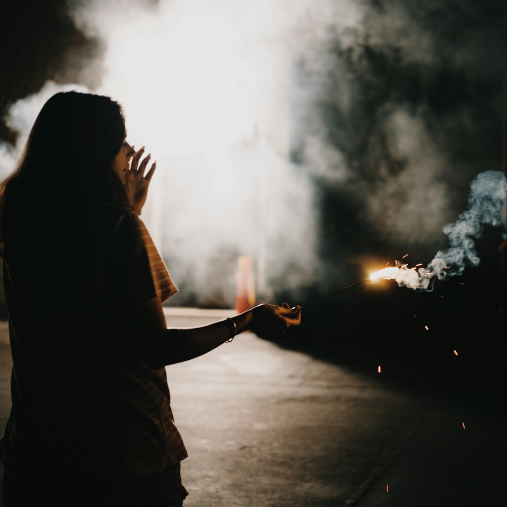 a woman standing in front of a fire with smoke coming out of it