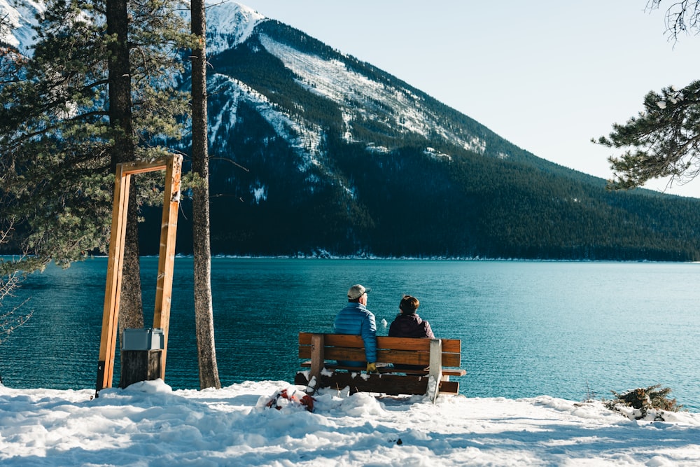 two people sitting on a bench overlooking a lake