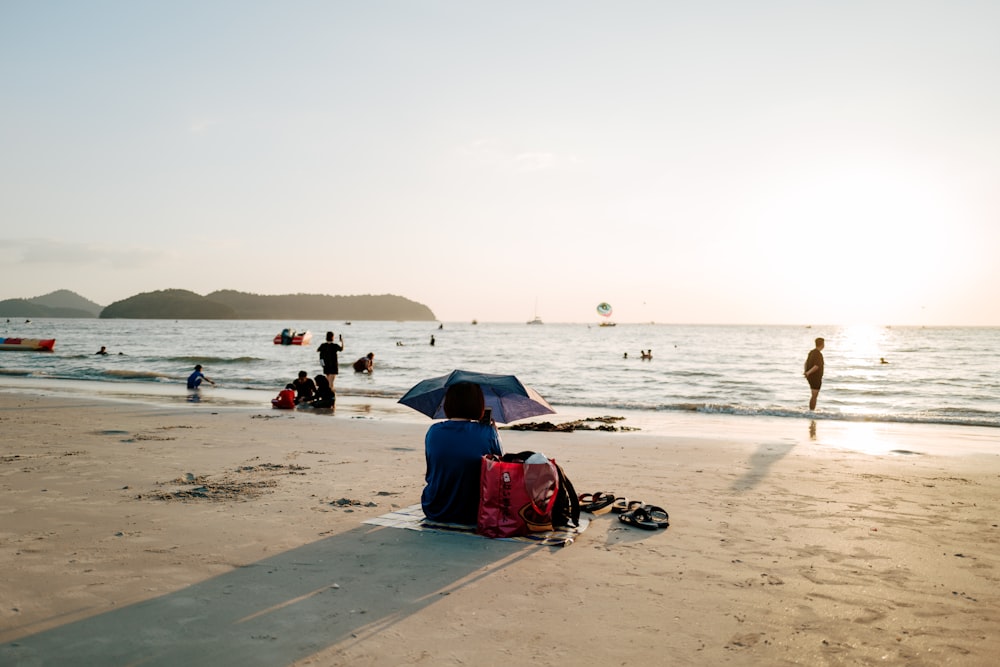 uma pessoa sentada na praia com um guarda-sol
