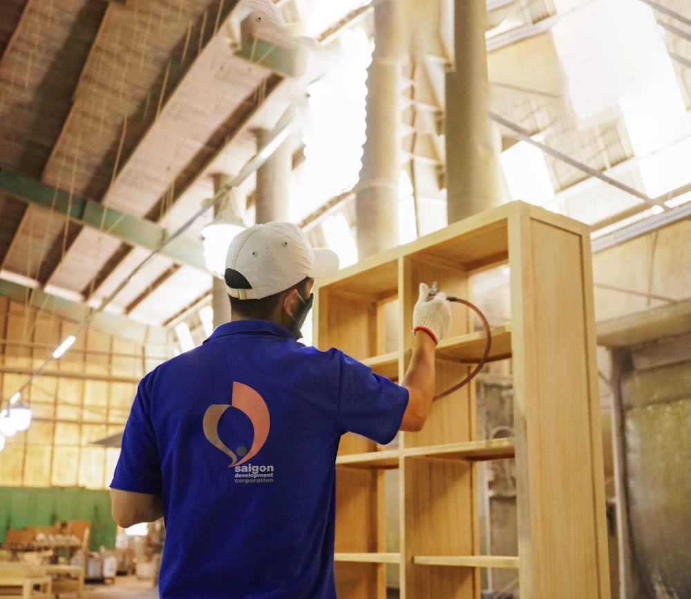 a man in a blue shirt and white hat working on a shelf