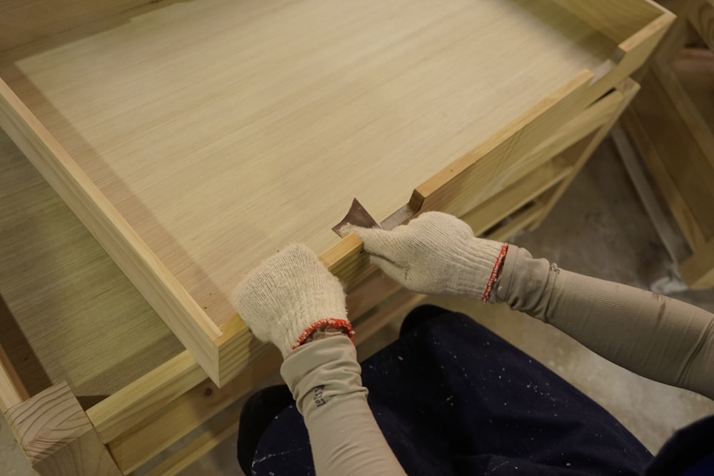 a person with a pair of gloves on working on a piece of wood