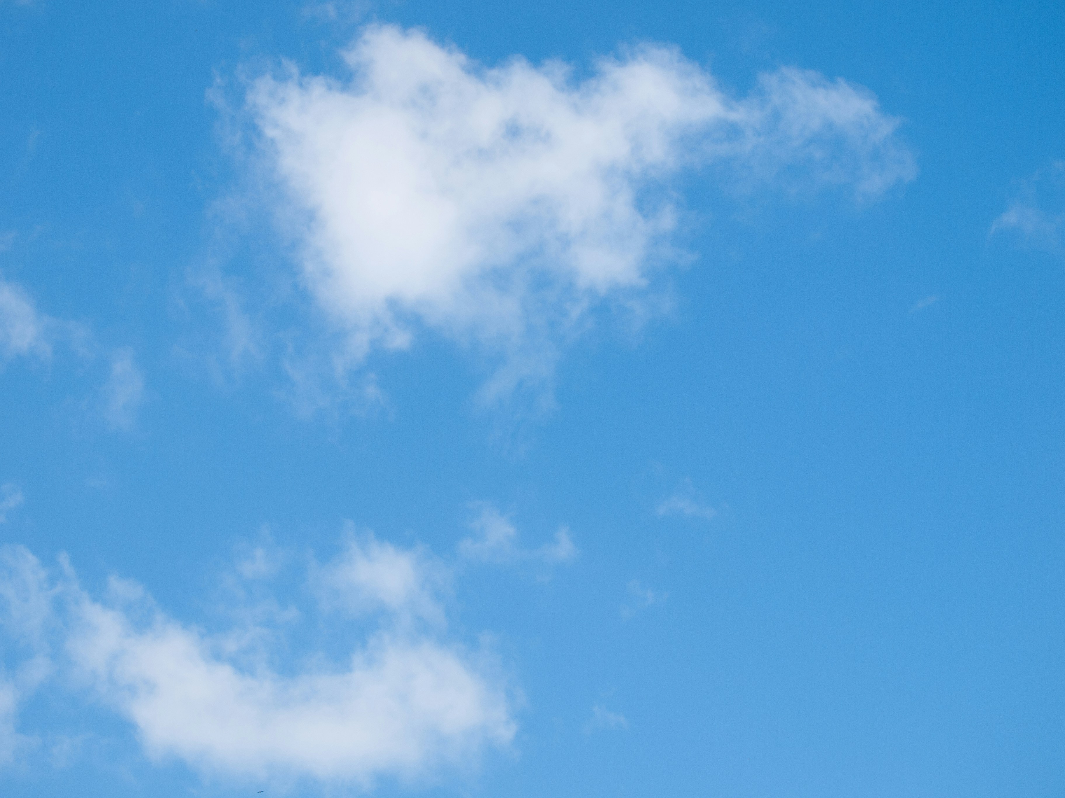 a plane flying in a blue sky with clouds