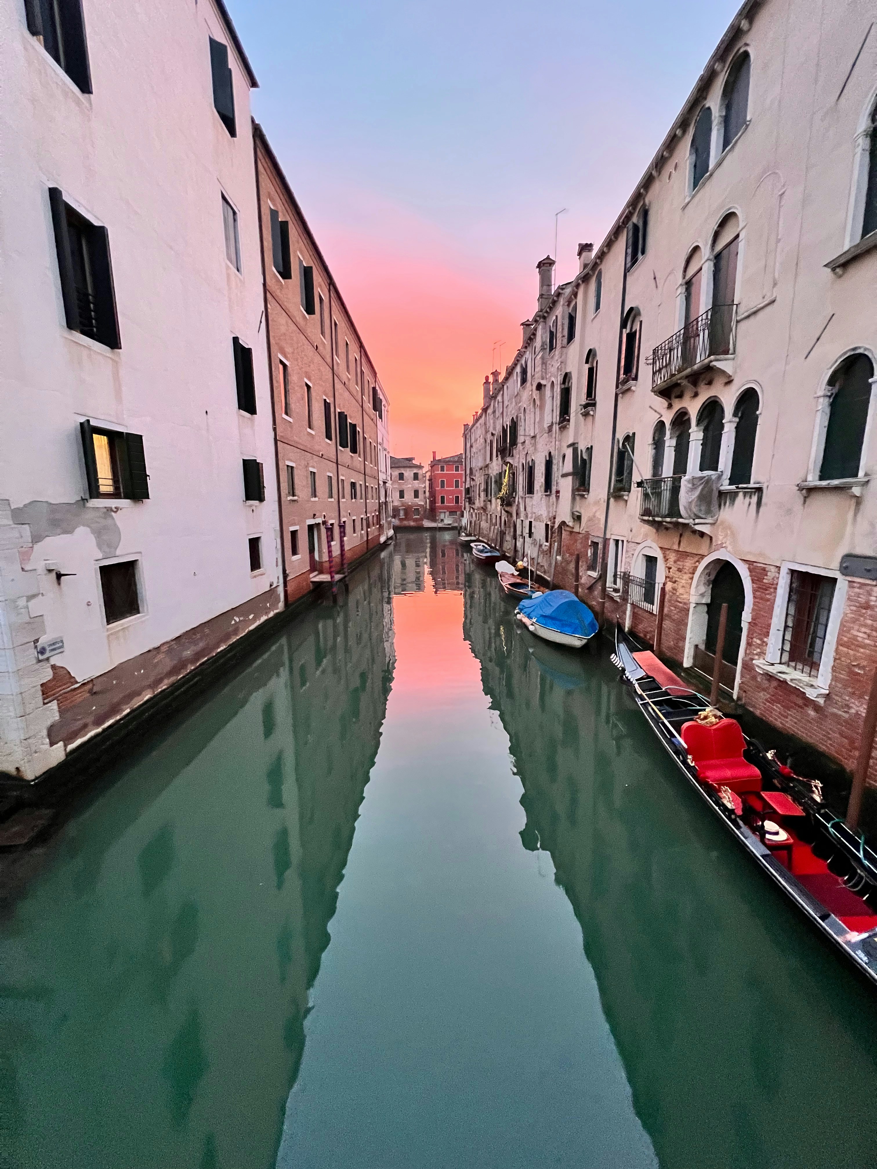 Canale veneziano con gondole al tramonto, riflessi dorati sull'acqua calma, palazzi storici color pastello sullo sfondo
