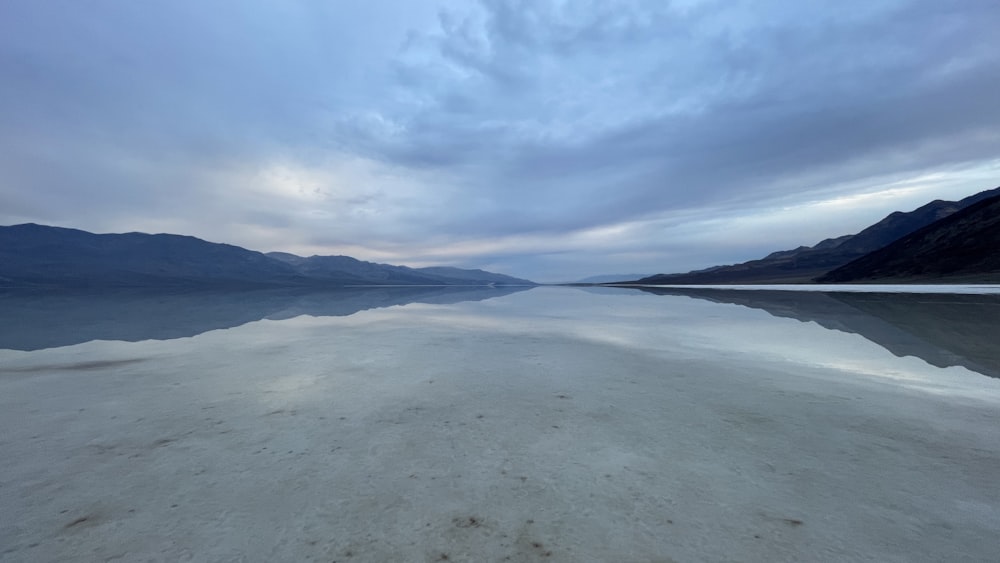 a body of water surrounded by mountains under a cloudy sky