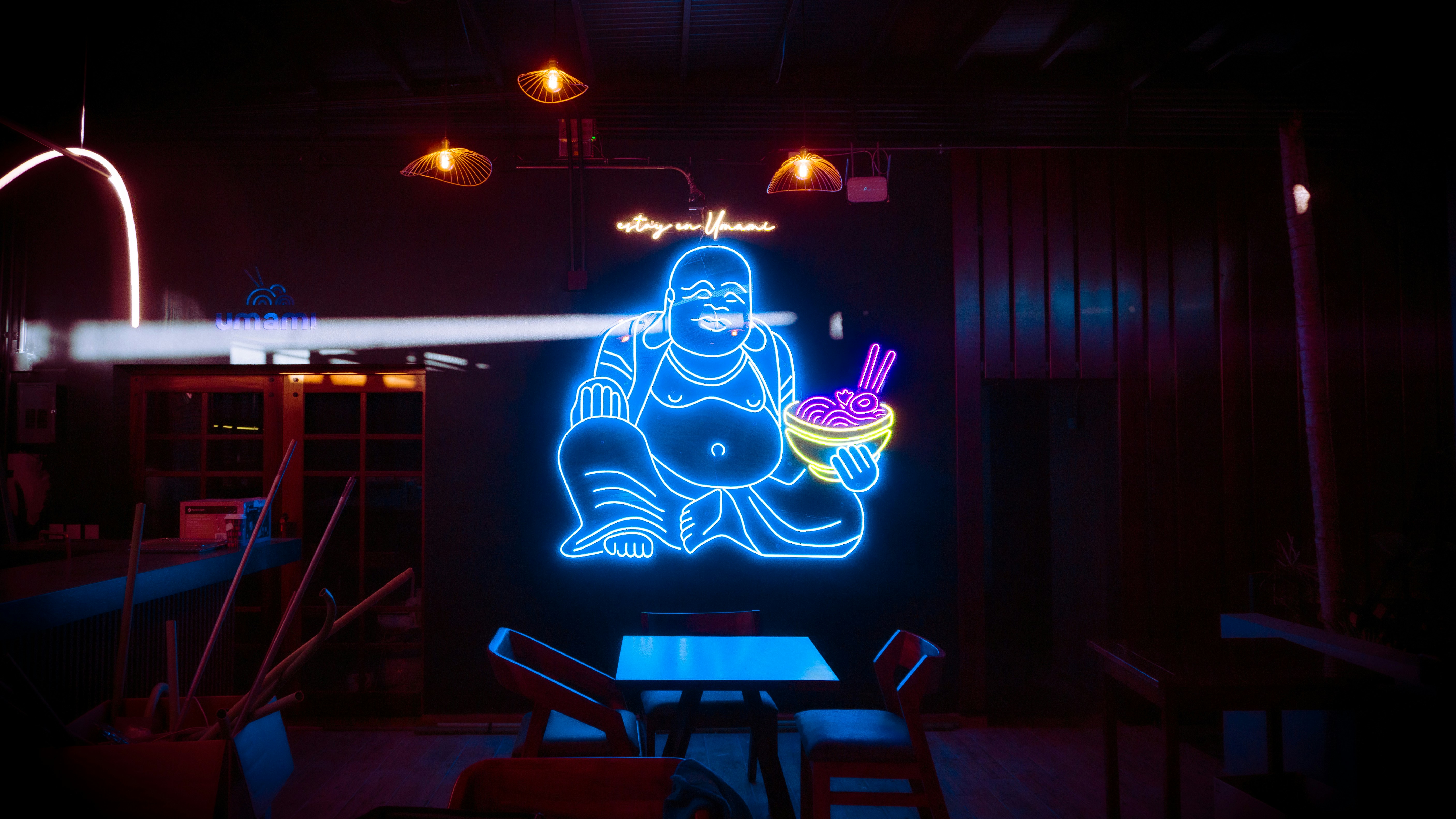 A neon sign of a buddha eating a bowl of noodles