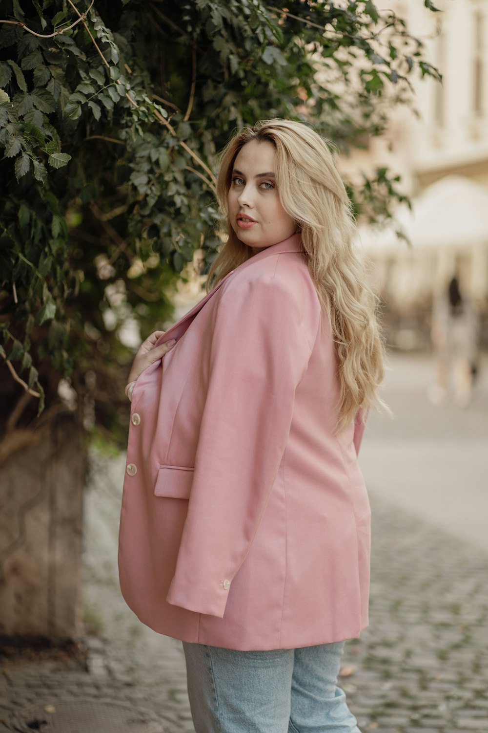 a woman in a pink jacket standing on a cobblestone street