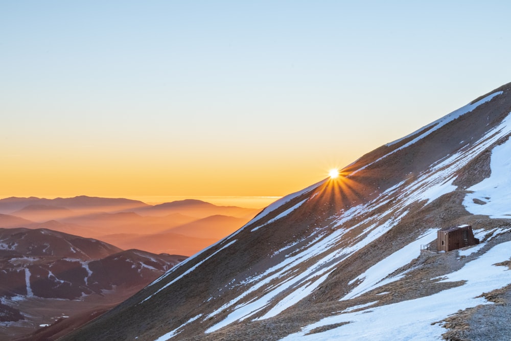 the sun is setting on a snowy mountain