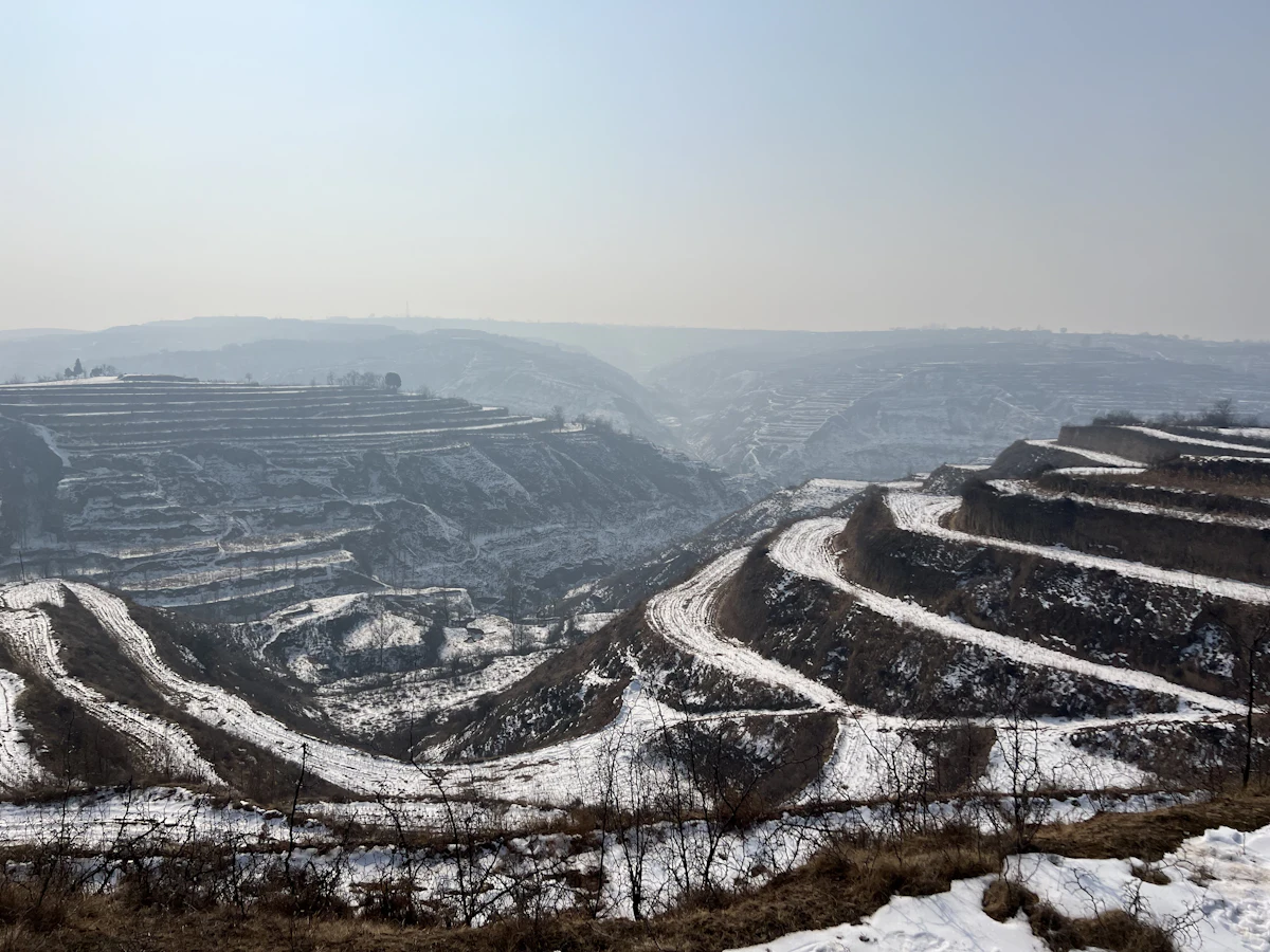 Loess terraces under snow in Fushan County, Linfen, with hazy ridges behind