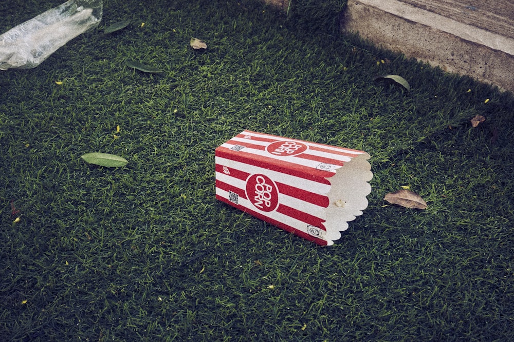 a red and white box sitting on top of a lush green field