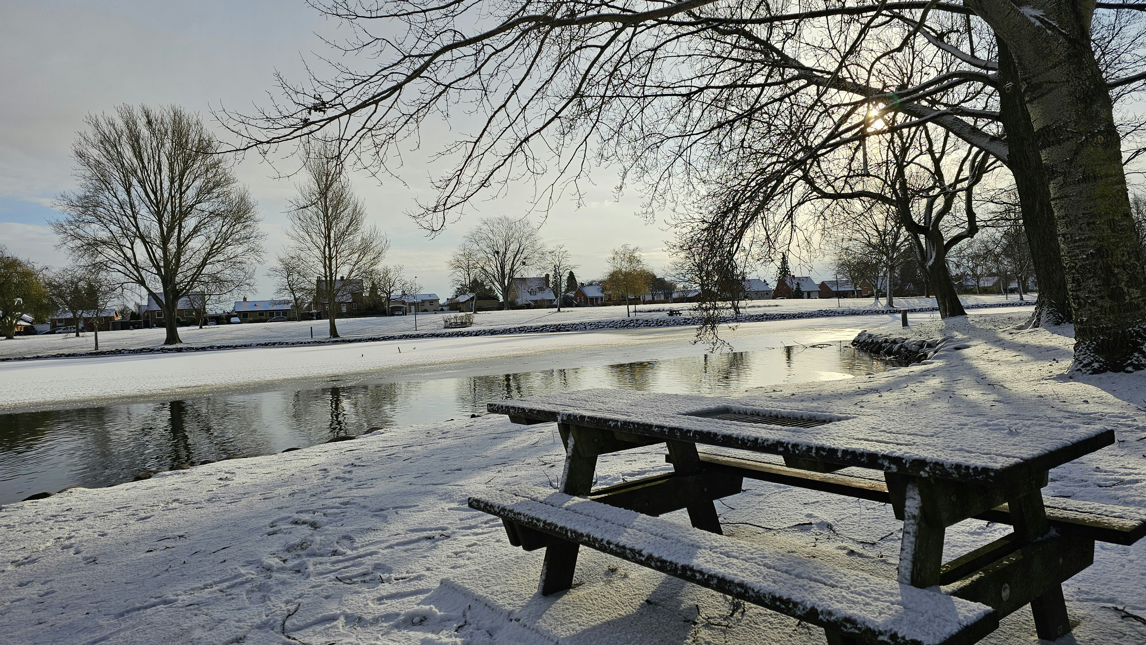 A park bench covered in snow next to a river photo – Free Grey Image on ...