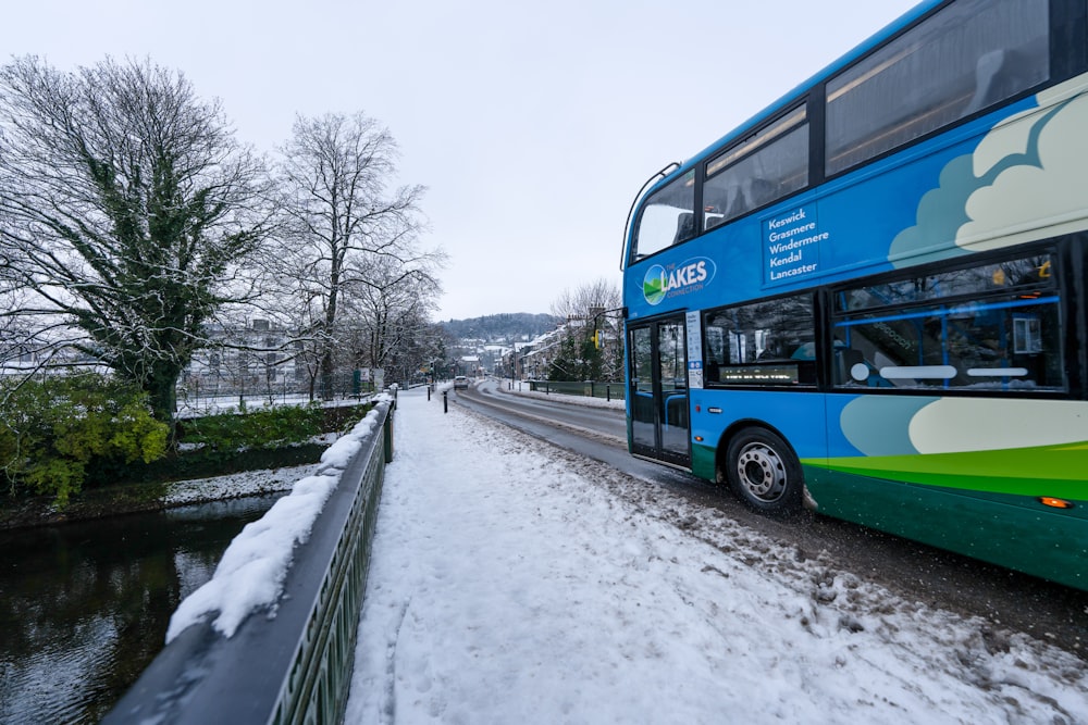 a blue double decker bus driving down a snow covered road