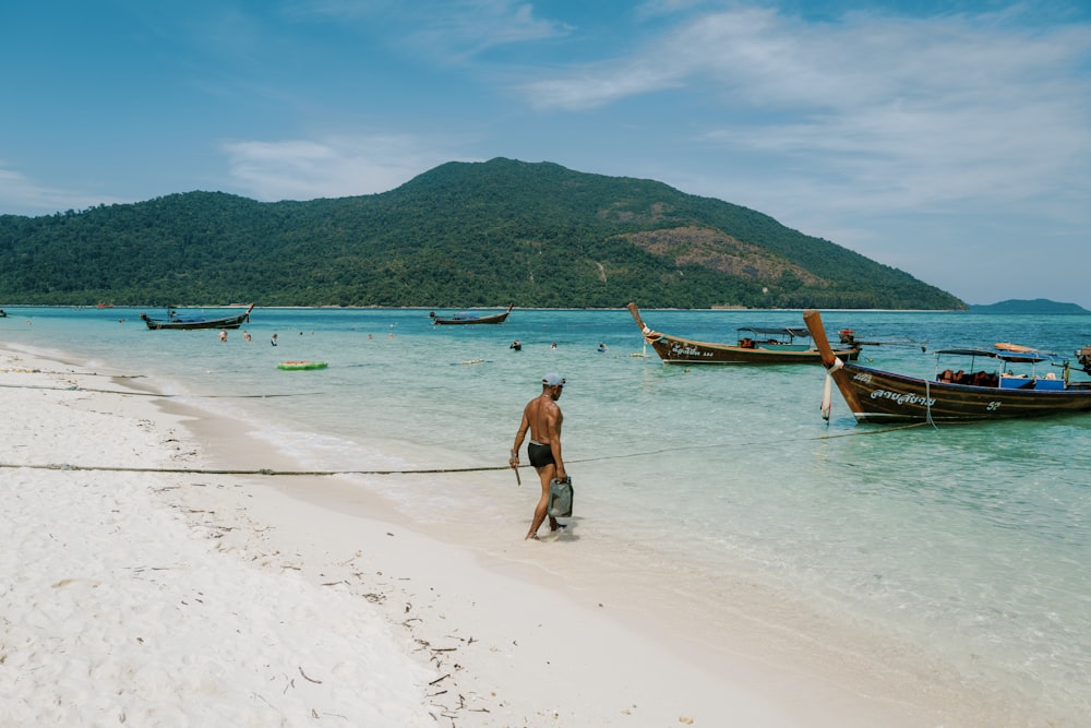 a man walking along a beach next to boats