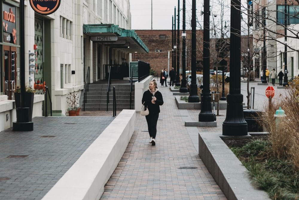 a woman walking down a sidewalk next to tall buildings