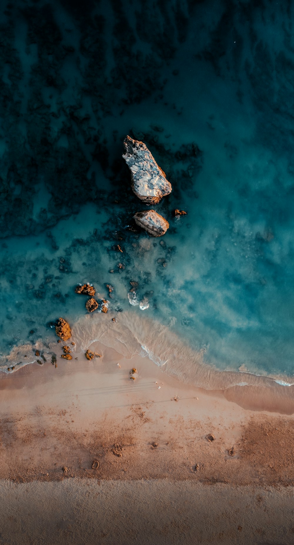 an aerial view of a beach with a rock in the water