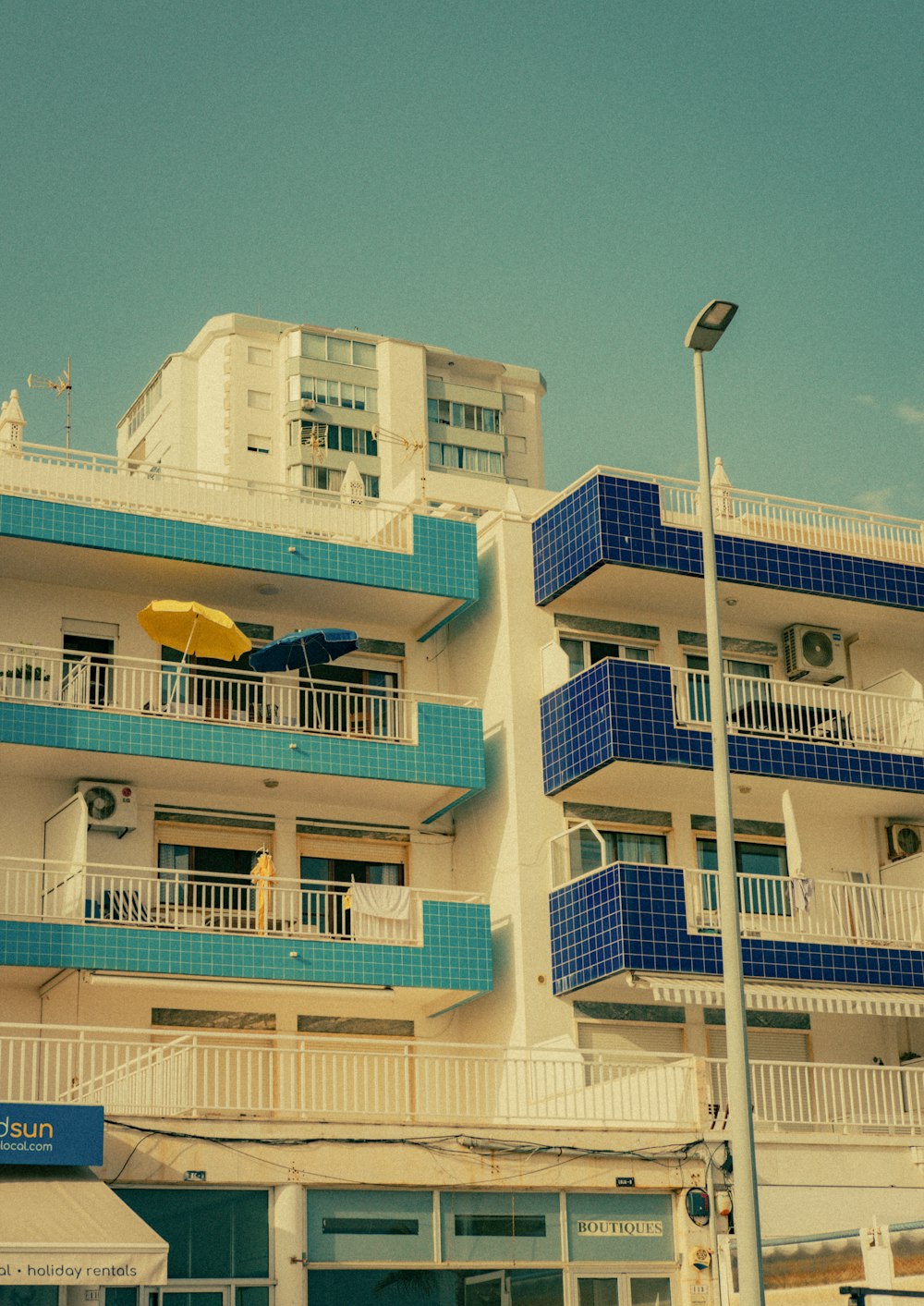 un bâtiment bleu et blanc avec des balcons et un parasol jaune