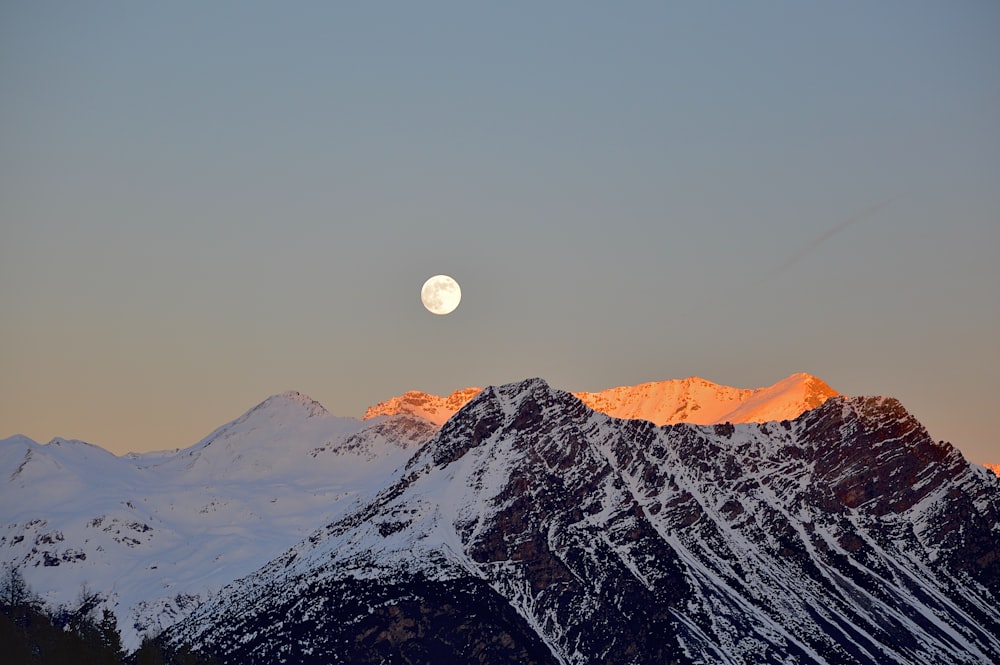 the moon is setting over a snowy mountain range