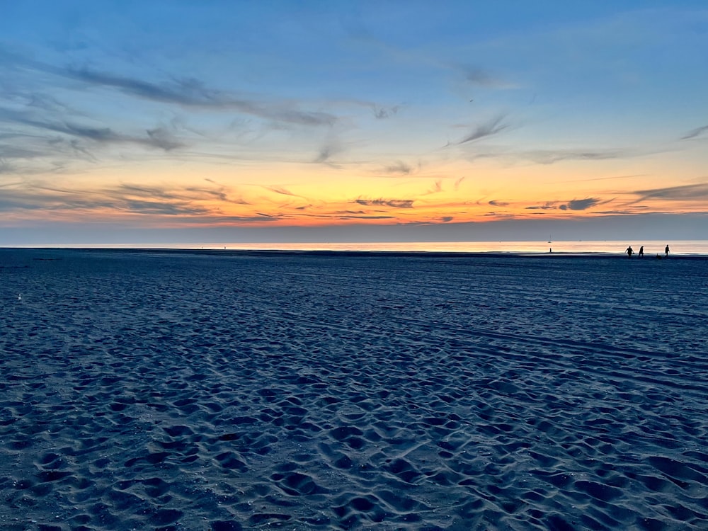 Die Sonne geht über dem Strand unter und die Menschen gehen darauf spazieren