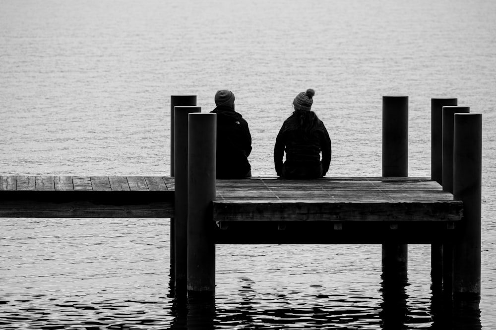 a couple of people sitting on top of a pier