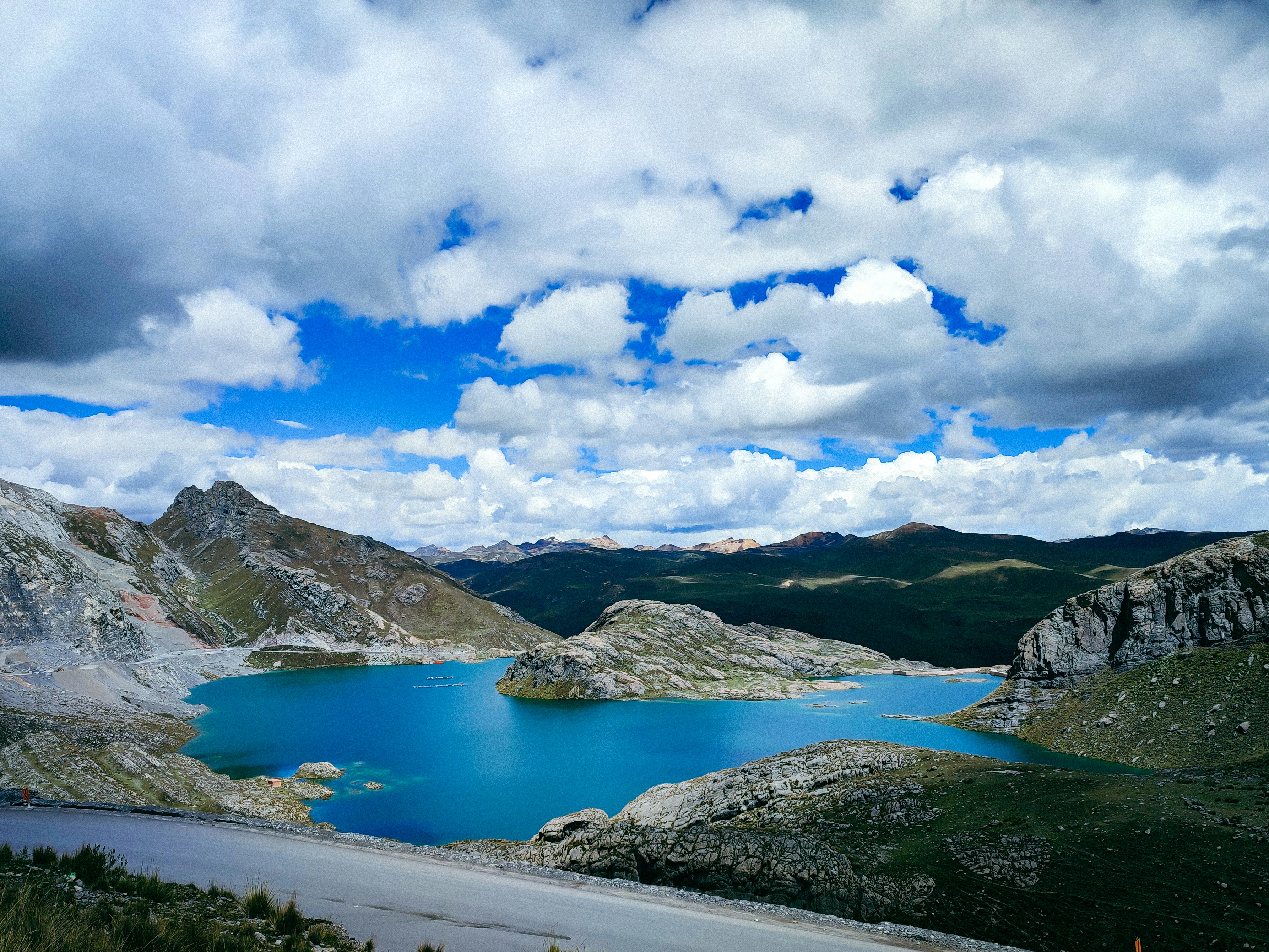 An asphalt road curves beside a turquoise mountain lake.