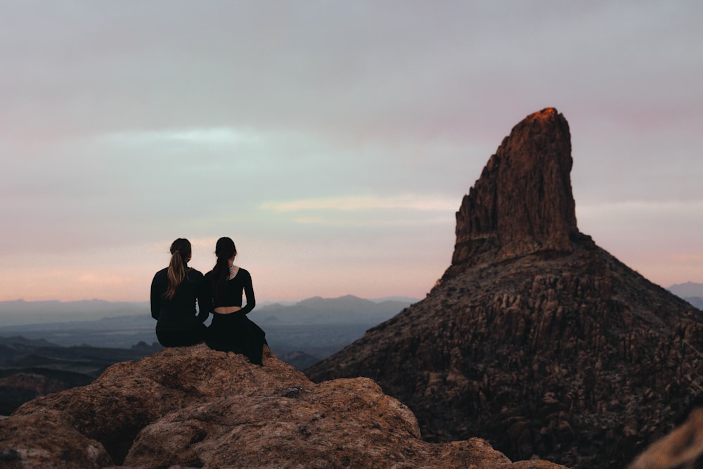 two people sitting on top of a large rock