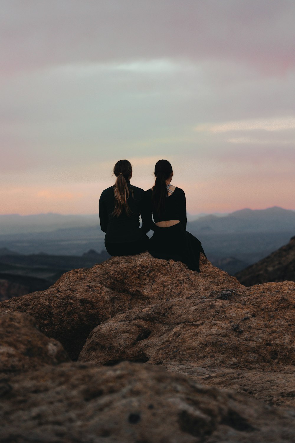 two people sitting on top of a large rock