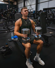 a man sitting in a gym holding two dumbs